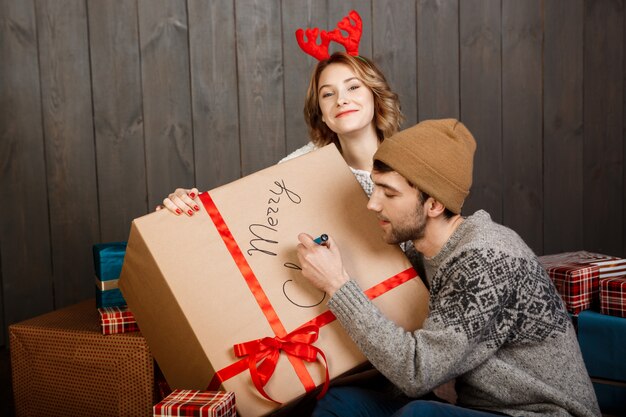 Man writing on gift box merry christmas sitting with womanfriend