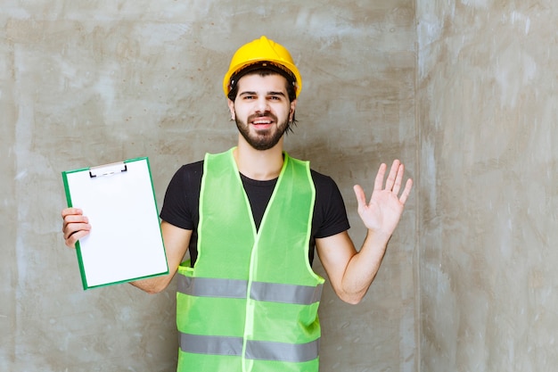 Free photo man in yellow helmet and gear holding a project plan and looks confused