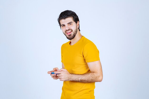 Man in yellow shirt holding a blue smartphone.