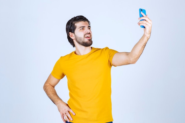 Man in yellow shirt holding a blue smartphone.