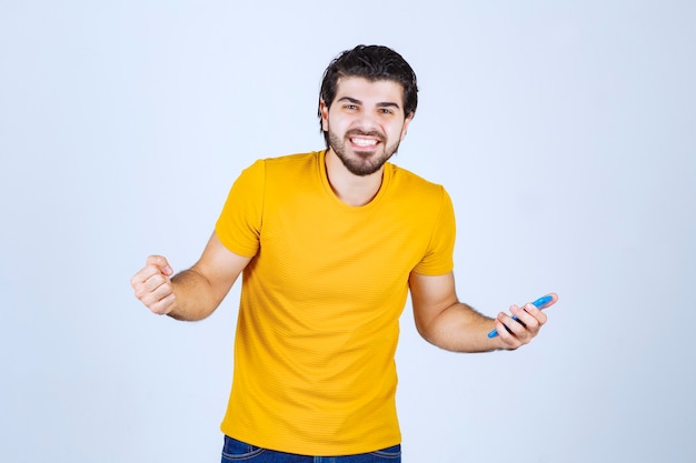 Man in yellow shirt pointing his smartphone and enjoying it.