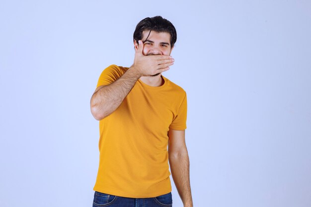 Man in yellow shirt putting hand to his face and laughing. 