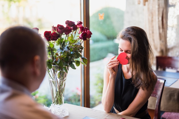 Man and young woman closing face by ornament heart at table