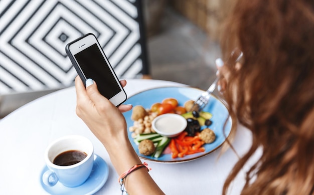 Free photo management diningout and people concept side shoulder view of woman hand using mobile phone checking messages while eating at restaurant or cafe contact client while at lunch