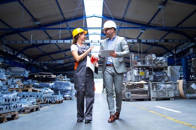 Manager supervisor and industrial worker in uniform walking in large metal factory hall and talking about increasing production