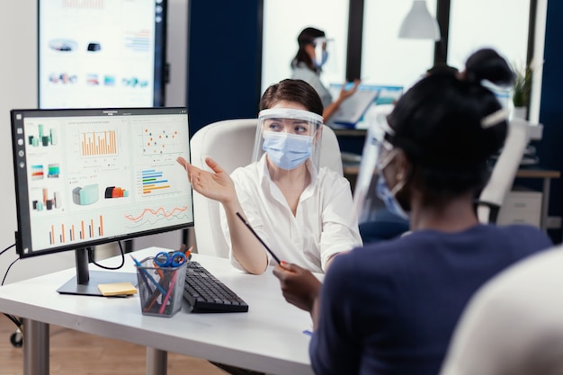 Free Photo manager wearing face mask for covid19 explaining financial graph to african employee. multiethnic team working in company with new normal respecting social distance because of global pandemic with cor