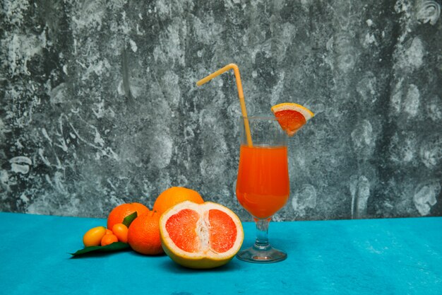 Mandarin oranges with orange and juice side view on blue textured table and gray texture