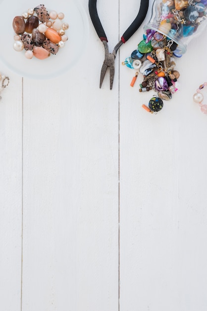 Many colorful beads and plier on wooden desk