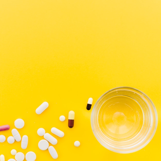 Free photo many pill and capsules near the glass of water on yellow backdrop