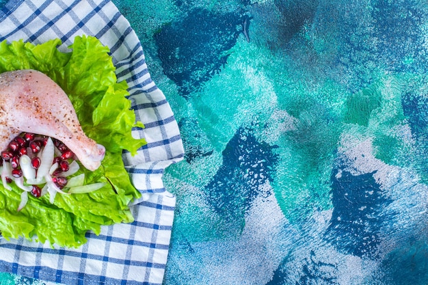 Marinated chicken drumstick with pomegranate arils on a lettuce leaves on a board on a tea towel on the blue background. High quality photo