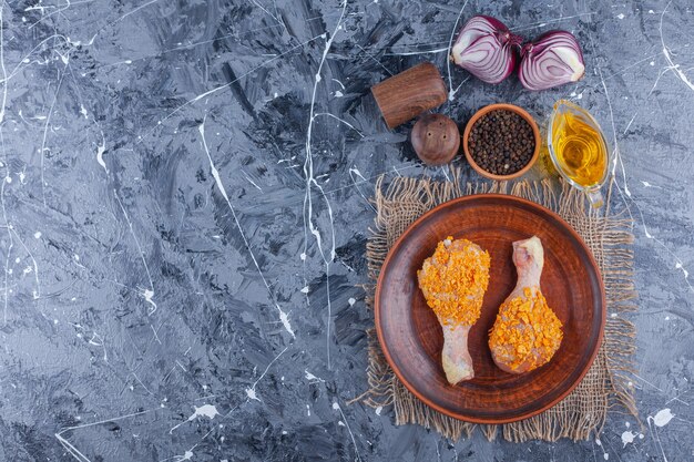 Marinated chicken drumsticks on a plate on a burlap next to spice and onion on the blue surface