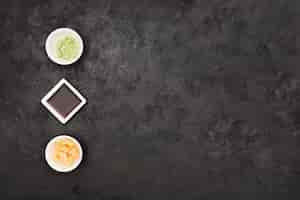 Free photo marinated ginger; soy sauce and wasabi bowl arranged in row over textured black surface