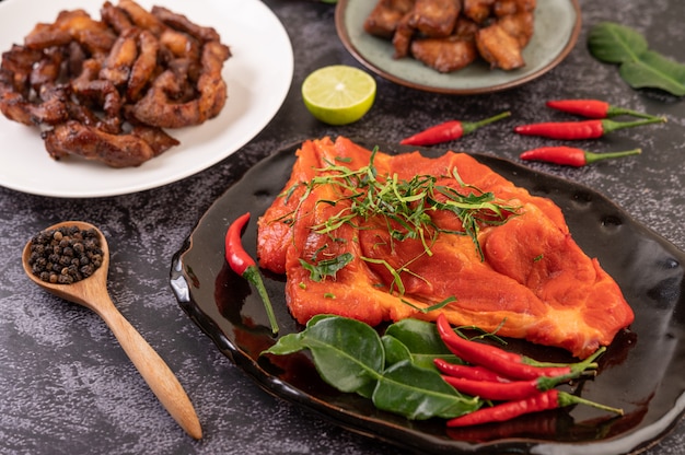 Marinated pork used in cooking, complete with chili peppers Kaffir lime leaves in a black plate