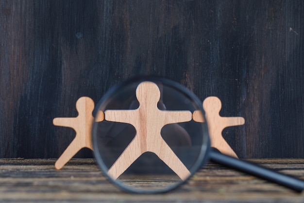 Marketing analysis concept with magnifying glass over wooden figure on wooden and grunge background close-up.