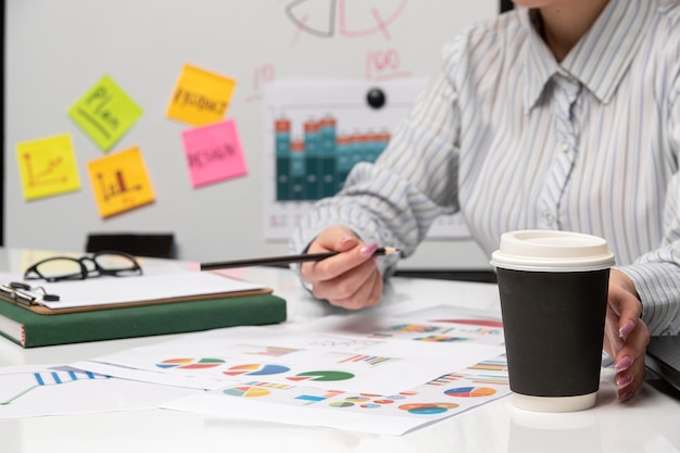 Marketing business lady in striped shirt in office with glasses on desk reaching coffee cup