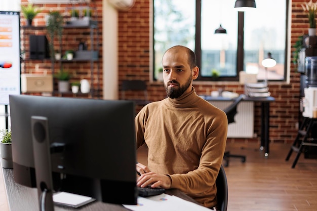 Marketing company employee sitting at desk, developing management plan while using work computer. Office worker with financial knowledge seeking business recovery solution while using desktop PC.