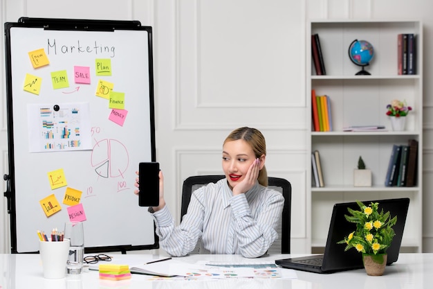 Free photo marketing smart cute business lady in striped shirt in office looking at cell phone