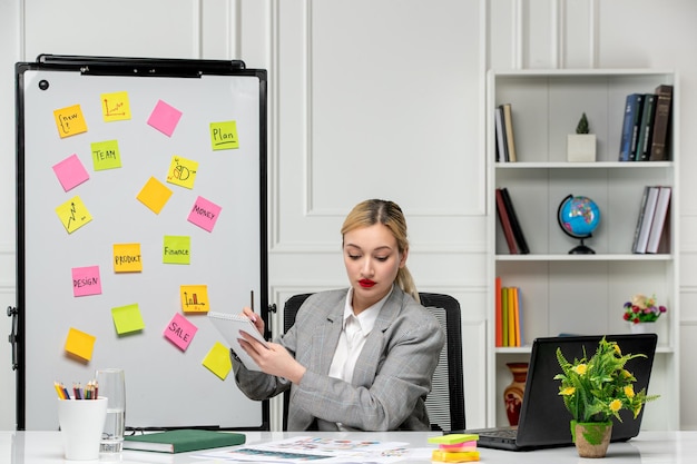 Free photo marketing young cute blonde girl in grey suit in the office writing down notes