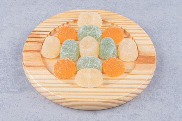 Marmelades neatly arranged on a wooden platter on marble table.