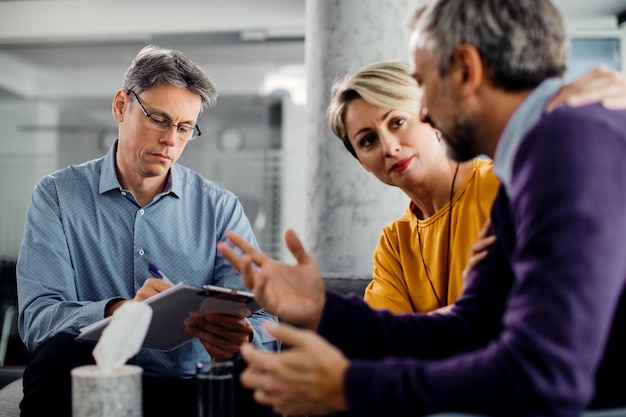 Marriage counselor taking notes while having meeting with a couple in the office