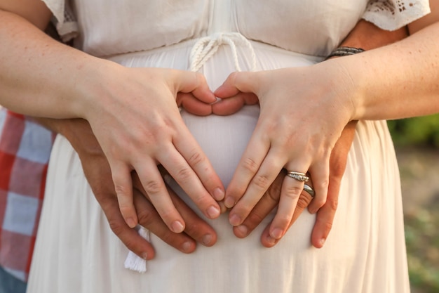 Married couple forming a heart shape with hands on the pregnant belly of the woman