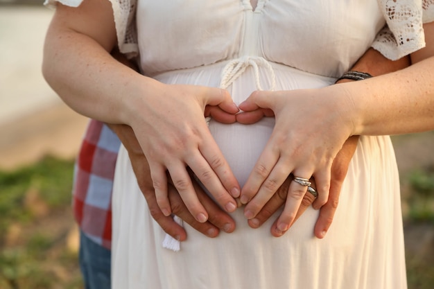 Married couple forming a heart shape with hands on the pregnant belly of the woman