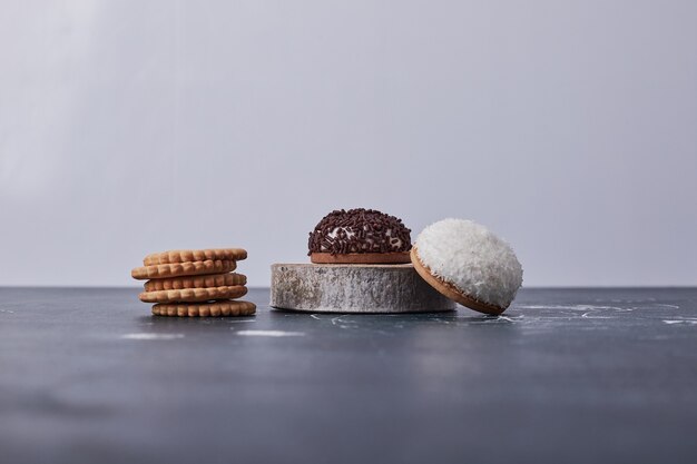 Marshmallow cookies with chocolate and coconut powder on a piece of wood on blue.