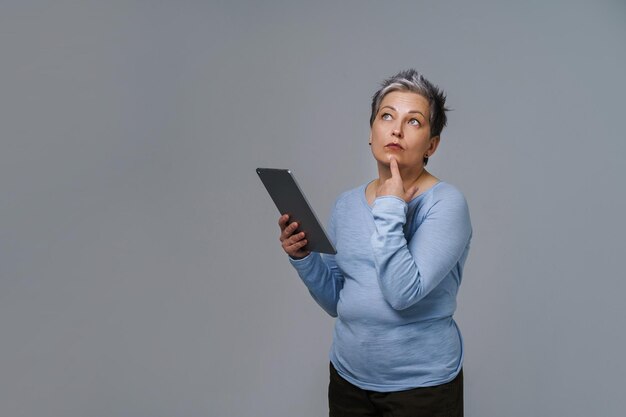 Marvelous mature woman 50s grey haired with digital tablet working or checking on social media Pretty woman in blue blouse isolated on white Older people and technologies Toned image