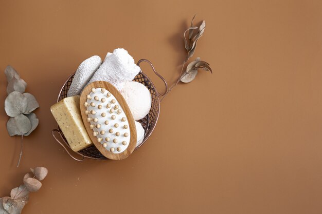 Massage brush, bath bombs, soap and towel in basket on brown background top view.