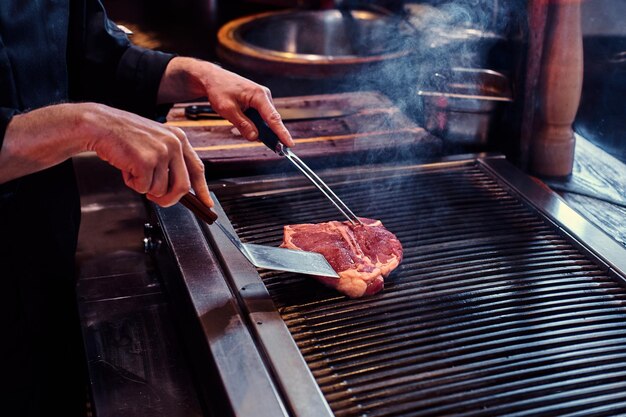 Master chef wearing uniform cooking delicious beef steak on a kitchen in a restaurant