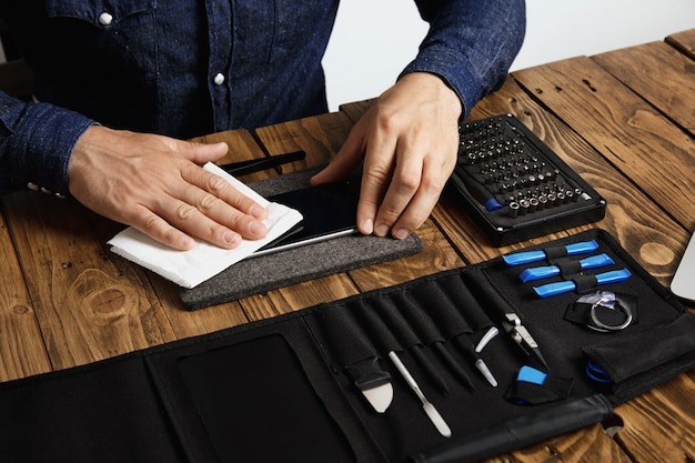 Free photo master cleans mobile phone after successful restoration with white cloth near his professional instruments in tool bag on wooden table