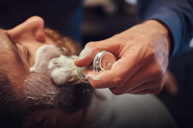 A master hairdresser prepares the face for shaving and smears the face with foam in a hairdressing salon.