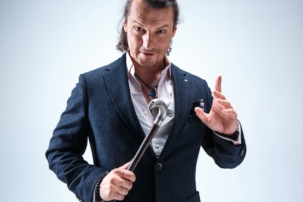 The mature bearded man in a suit holding cane. Isolated on a blue studio.