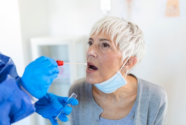 Free photo mature caucasian woman in a clinical setting being swabbed by a healthcare worker in protective garb to determine if she has contracted the coronavirus or covid19