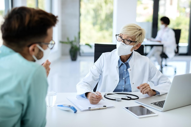 Free photo mature doctor wearing face mask while talking to a patient at medical clinic