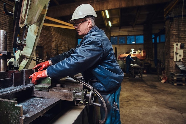 Free photo mature experienced worker is cutting metal using a special machine tool.