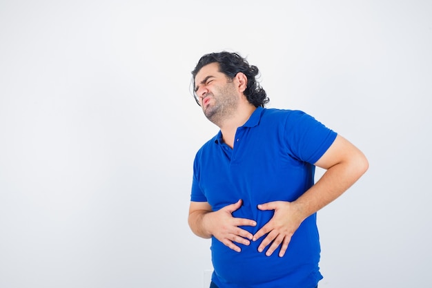 Mature man in blue t-shirt suffering from stomachache and looking painful , front view.