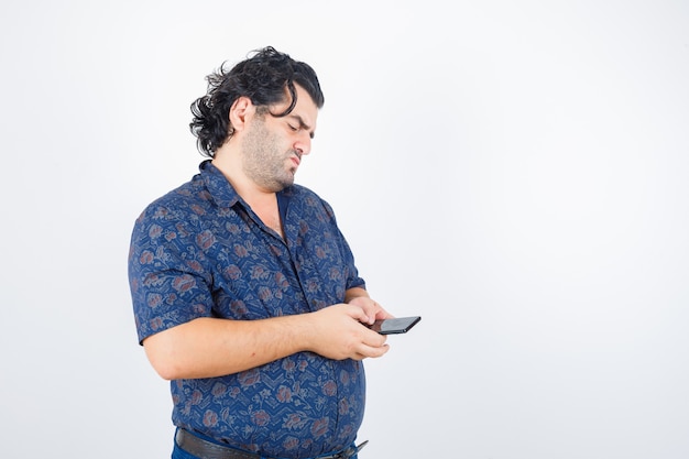 Mature man looking at mobile phone in shirt and looking pensive , front view.