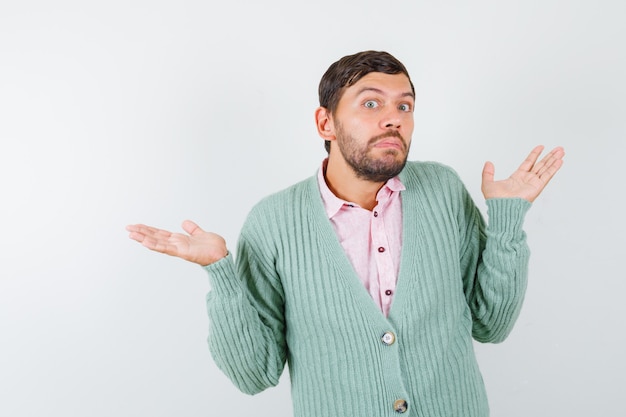 Mature man showing helpess gesture in shirt, cardigan and looking puzzled , front view.