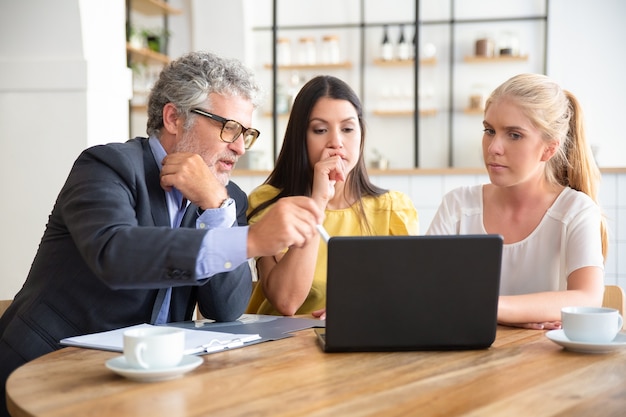 Mature professional explaining project details to young customers, pointing at pc display