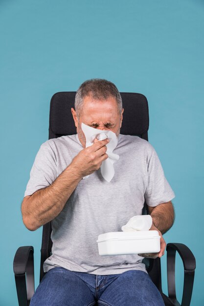 Mature sick man blowing his nose with tissue