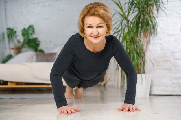 Mature woman in black sportswear doing push-ups at home. Healthy lifestyle concept