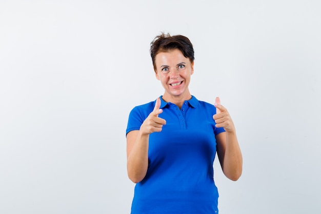 Mature woman in blue t-shirt pointing at camera and looking confident , front view.