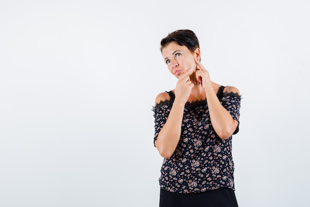 Free Photo mature woman in floral blouse, black skirt checking skin and looking focused , front view.