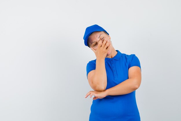 Mature woman holding hand on face in blue t-shirt and looking disappointed.