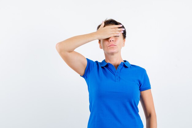 Mature woman holding hand on forehead in blue t-shirt and looking pensive. front view.