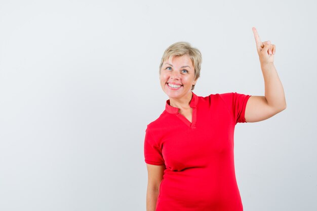 Mature woman pointing up in red t-shirt and looking confident.