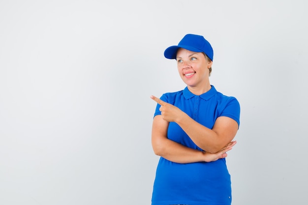 Mature woman pointing at upper left corner in t-shirt and looking cheery.