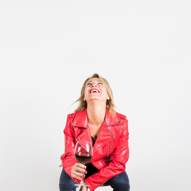 Mature woman in red jacket holding wine glass looking up laughing against white backdrop