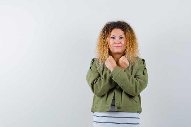 Mature woman showing protest gesture in green jacket, t-shirt and looking confident , front view.